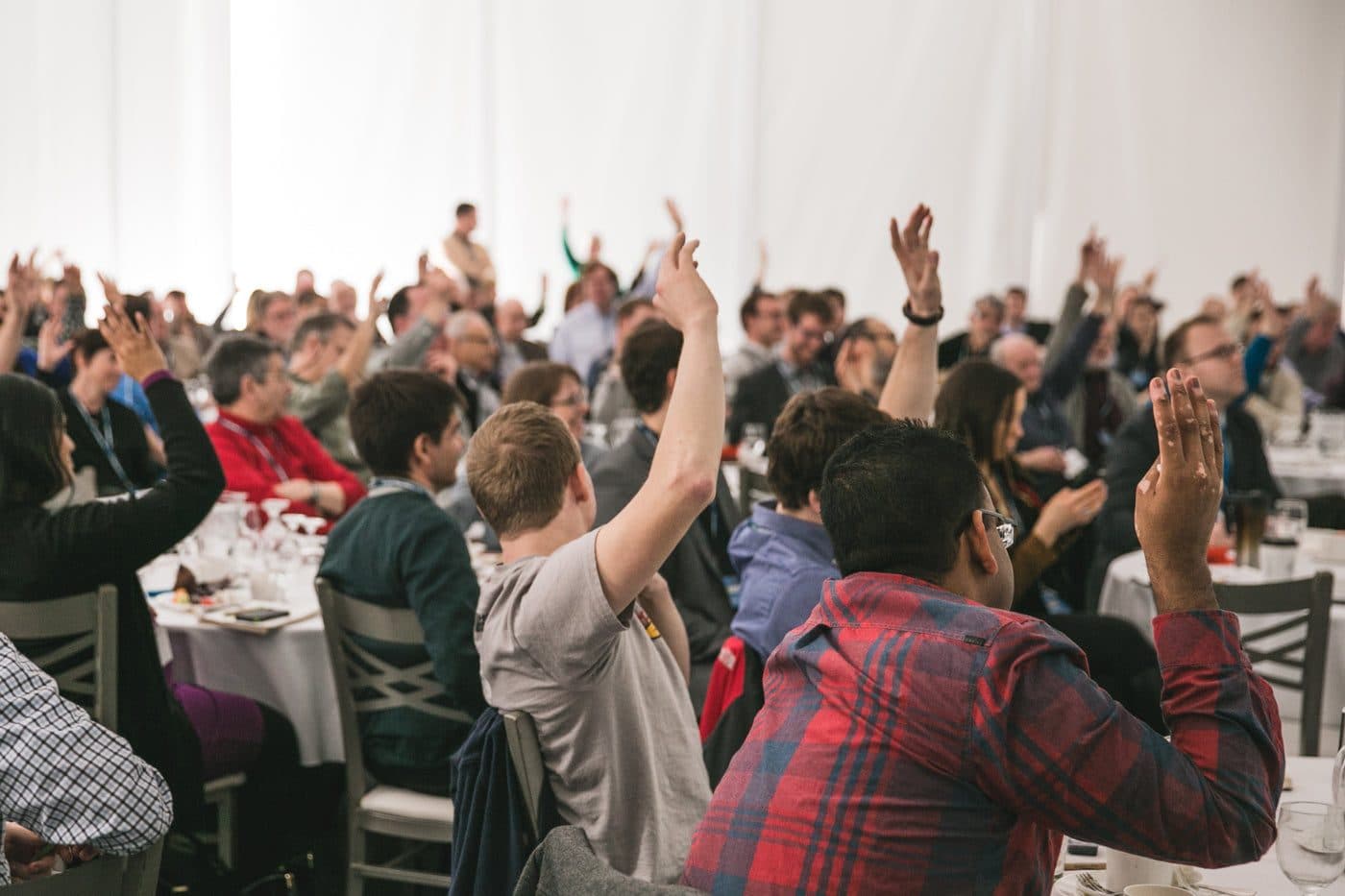 Une salle pleine pendant un événement d’entreprise, des participants lèvent la main