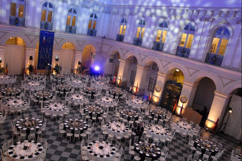 Grande salle de réception dressée pour une soirée de gala, tables rondes et éclairage violet