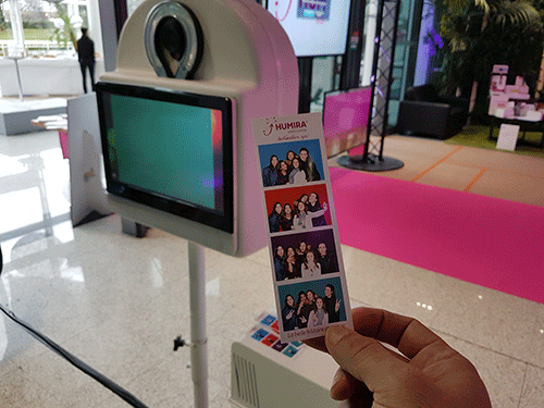 Main tenant une bande photo souvenir devant une borne photomaton rose en événement